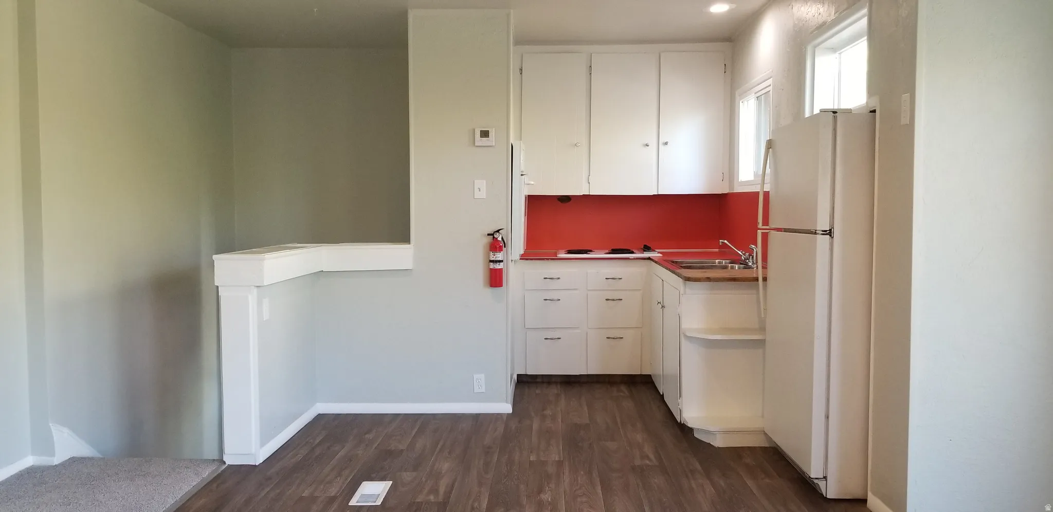 Compact kitchen featuring white cabinetry, a red backsplash, and wood-finish flooring