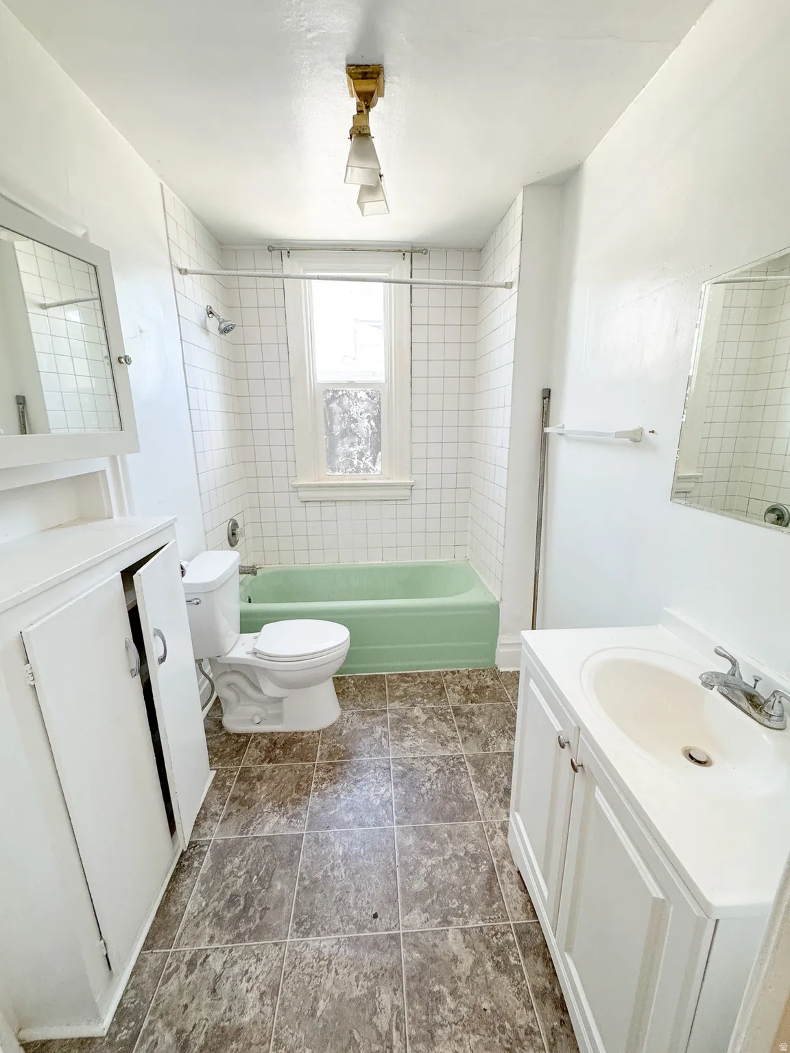Bathroom featuring a green bathtub, white subway tile shower surround, window with textured glass, wood-finish flooring, and a vanity with an integrated sink