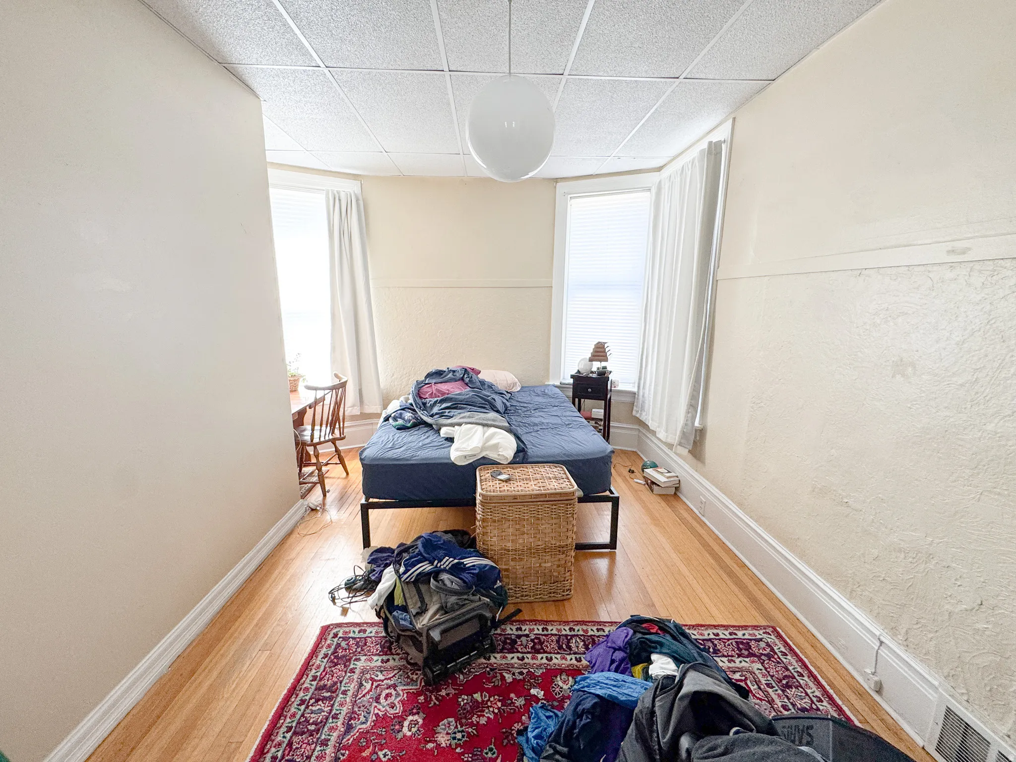 Spacious room featuring wood-finish flooring, light-colored walls, and a drop ceiling with a central globe light fixture