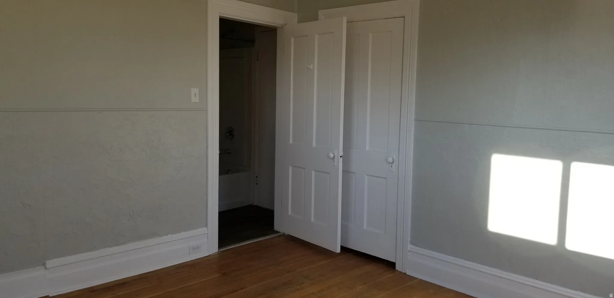 Hardwood flooring throughout a room with light gray painted walls and white trim