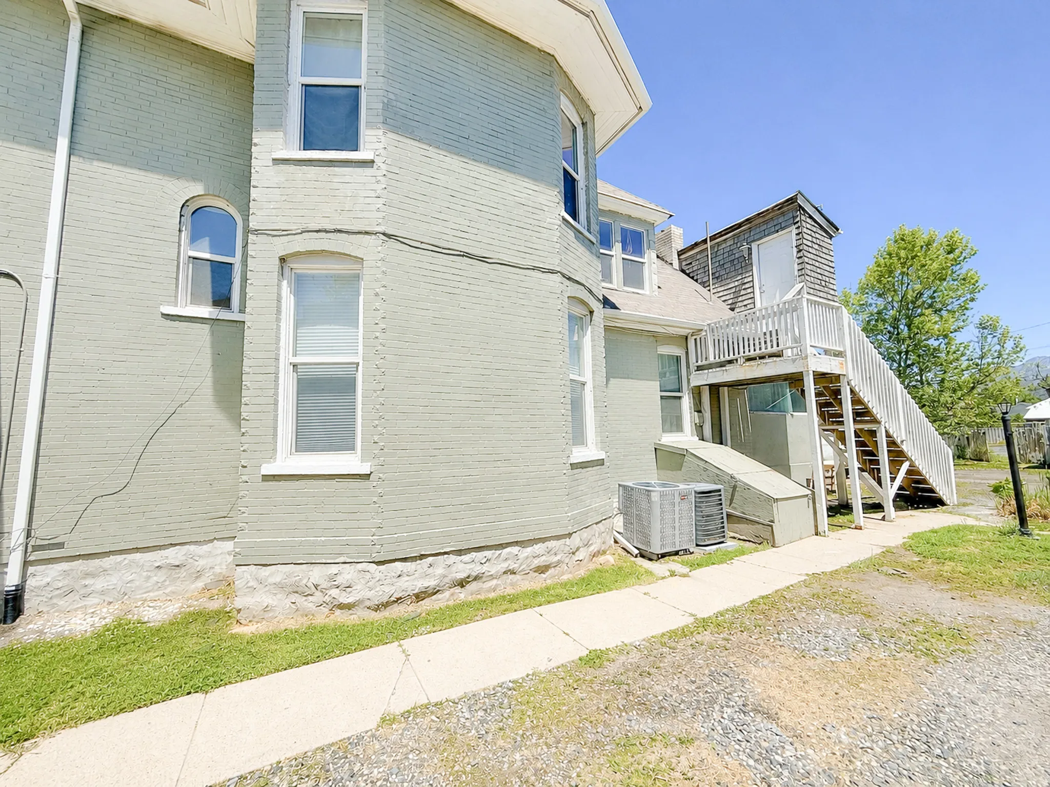 Exterior features include a light-colored brick facade, multiple window styles, a raised foundation, an external staircase with a landing, and an air conditioning unit