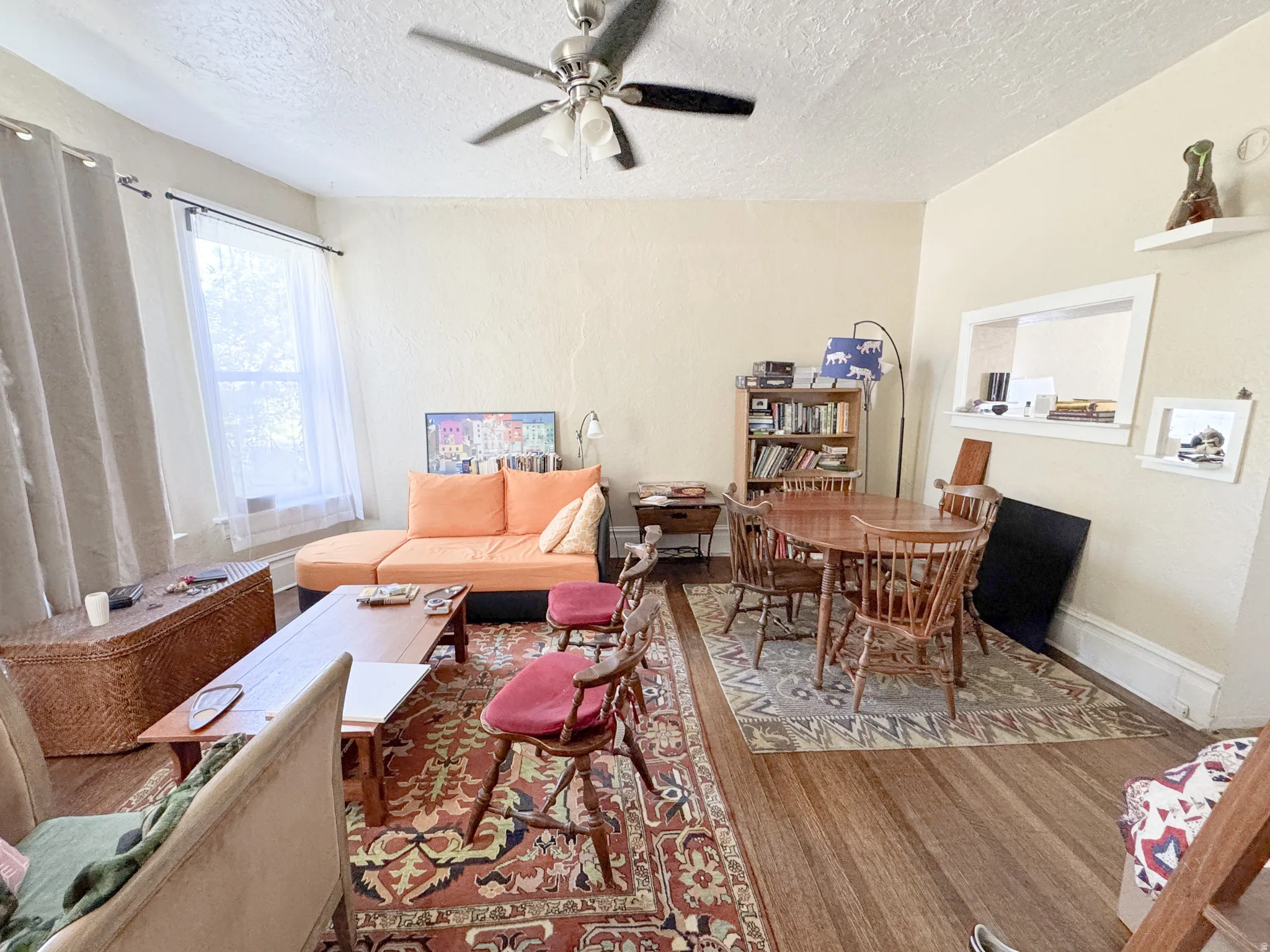 Bright living area featuring wood-finish flooring, a ceiling fan, and ample natural light from a large window