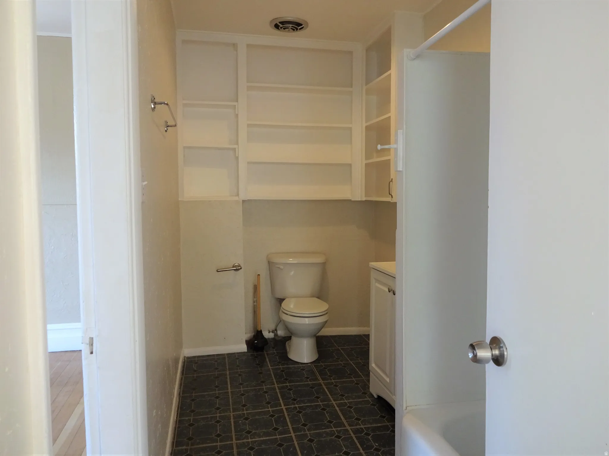 Bathroom featuring built-in white shelving, a toilet, a white vanity with cabinetry, and patterned floor tiles