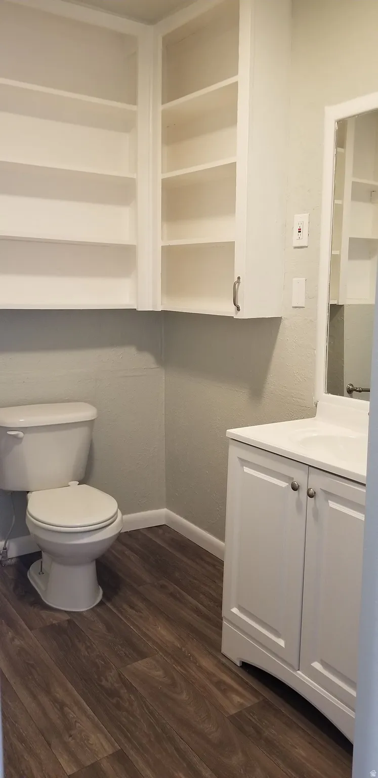 Bathroom featuring a white vanity with integrated sink, toilet, and wood-finish flooring