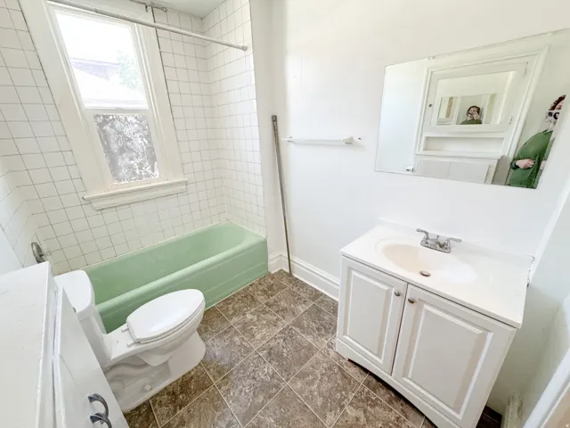 Bathroom featuring a green bathtub, white subway-style wall tile, a window with natural light, a vanity with an integrated sink, and a mirrored medicine cabinet