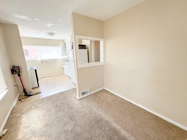 Carpeted interior space featuring a pass-through window to the kitchen, light-toned walls, and white baseboards