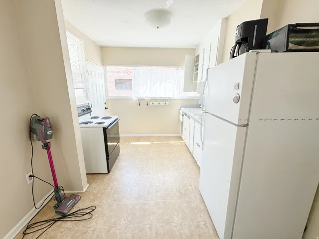 Kitchen featuring white appliances, white cabinetry, light-toned flooring, and a window with natural light