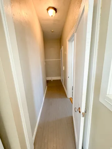 Hallway featuring wood-finish flooring, white trim, and a ceiling-mounted light fixture