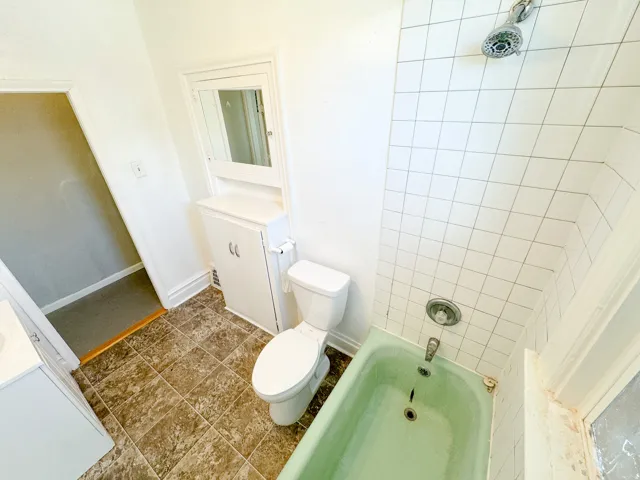 Bathroom featuring a green bathtub with a shower fixture, white tile surround, and a white toilet
