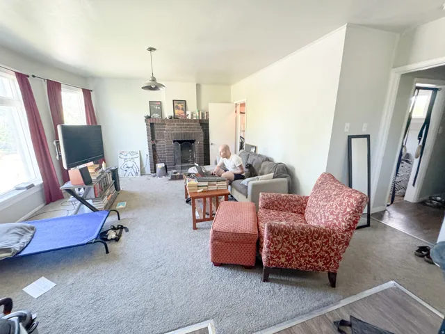 Living area featuring a brick fireplace, light-colored carpeting, multiple windows, a ceiling-mounted light fixture, and crown molding