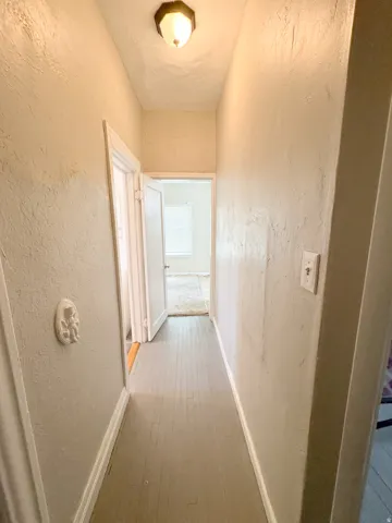 Hallway featuring wood-finish flooring, textured walls, and a ceiling-mounted light fixture