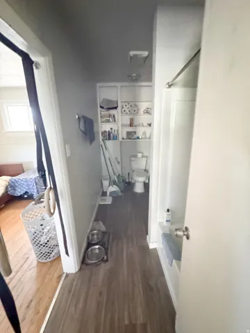 Compact bathroom featuring wood-finish flooring, a white toilet, and built-in shelving