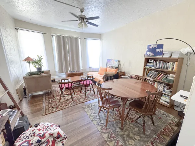 Spacious room featuring wood-finish flooring, a ceiling fan, and multiple windows