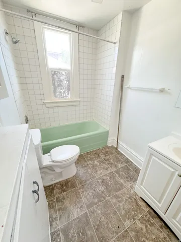Bathroom featuring a green bathtub with white subway tile surround, a single window, and a white toilet