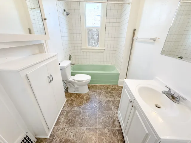 Bathroom featuring a green bathtub, white subway tile shower surround, and a white vanity with integrated sink