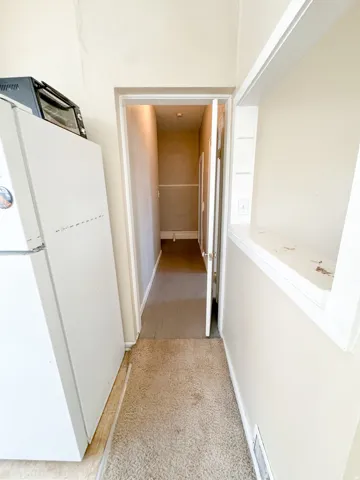 Hallway with light-colored walls and carpeted flooring, featuring a built-in shelving unit and an open doorway revealing additional interior space