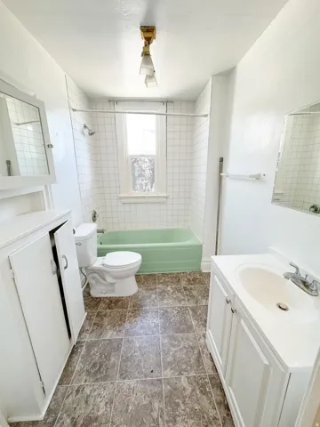 Bathroom featuring a green bathtub, white subway tile shower surround, window with textured glass, wood-finish flooring, and a vanity with an integrated sink