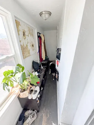 Narrow hall with wood-finish flooring, white painted walls, and a window providing natural light