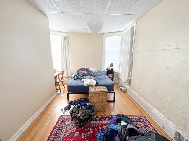 Spacious room featuring wood-finish flooring, light-colored walls, and a drop ceiling with a central globe light fixture