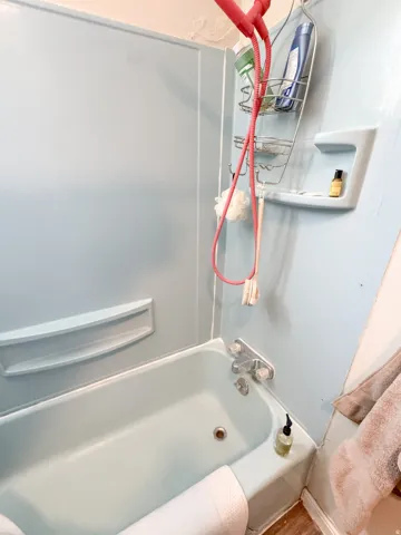Bathtub with integrated shower surround, featuring a built-in soap dish and chrome fixtures