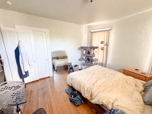 Hardwood flooring, white painted walls, and a window with light-filtering curtains