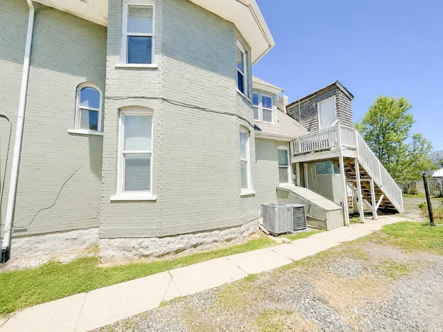 Exterior features include a light-colored brick facade, multiple window styles, a raised foundation, an external staircase with a landing, and an air conditioning unit