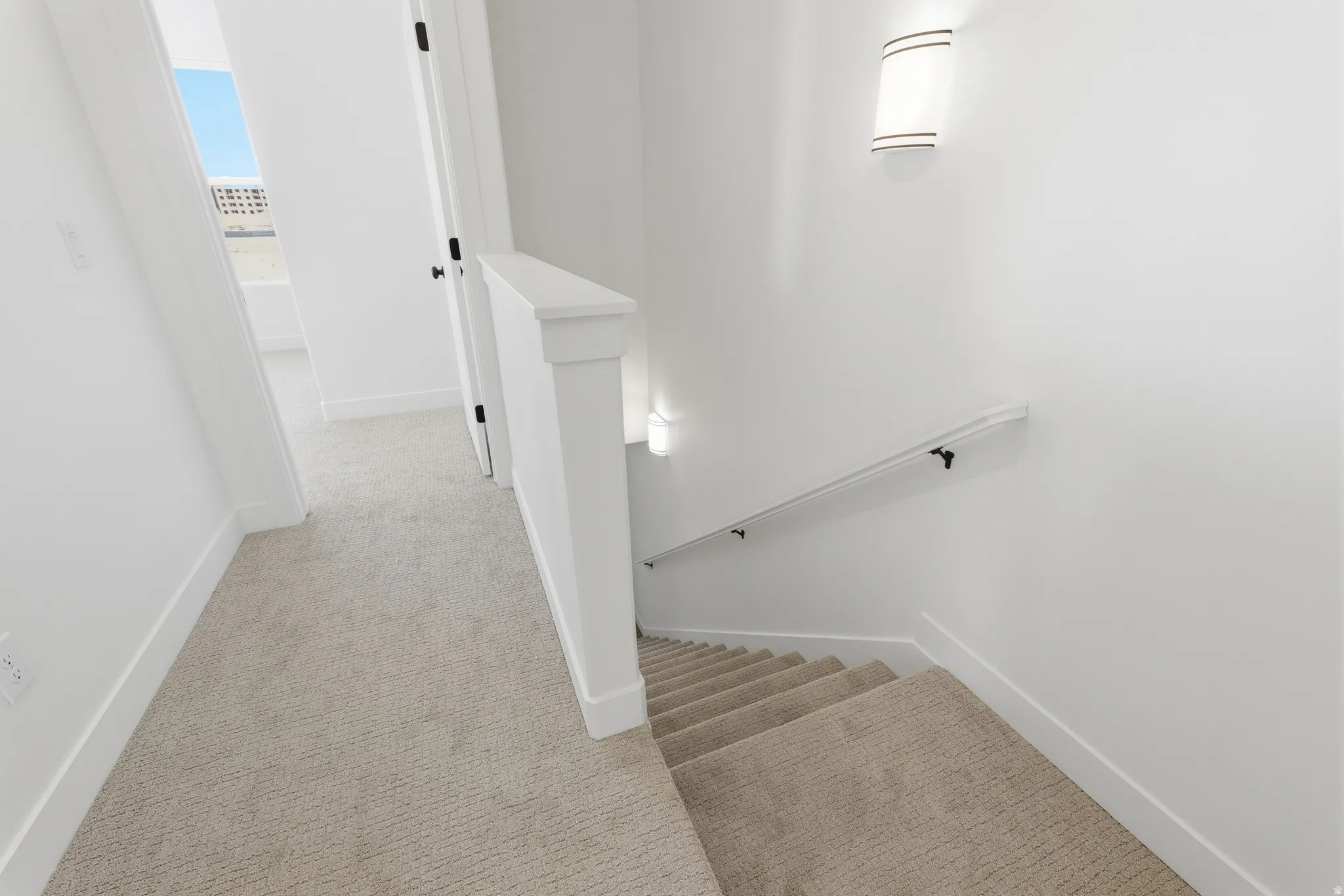 Carpeted staircase with white handrail and wall-mounted sconce lighting