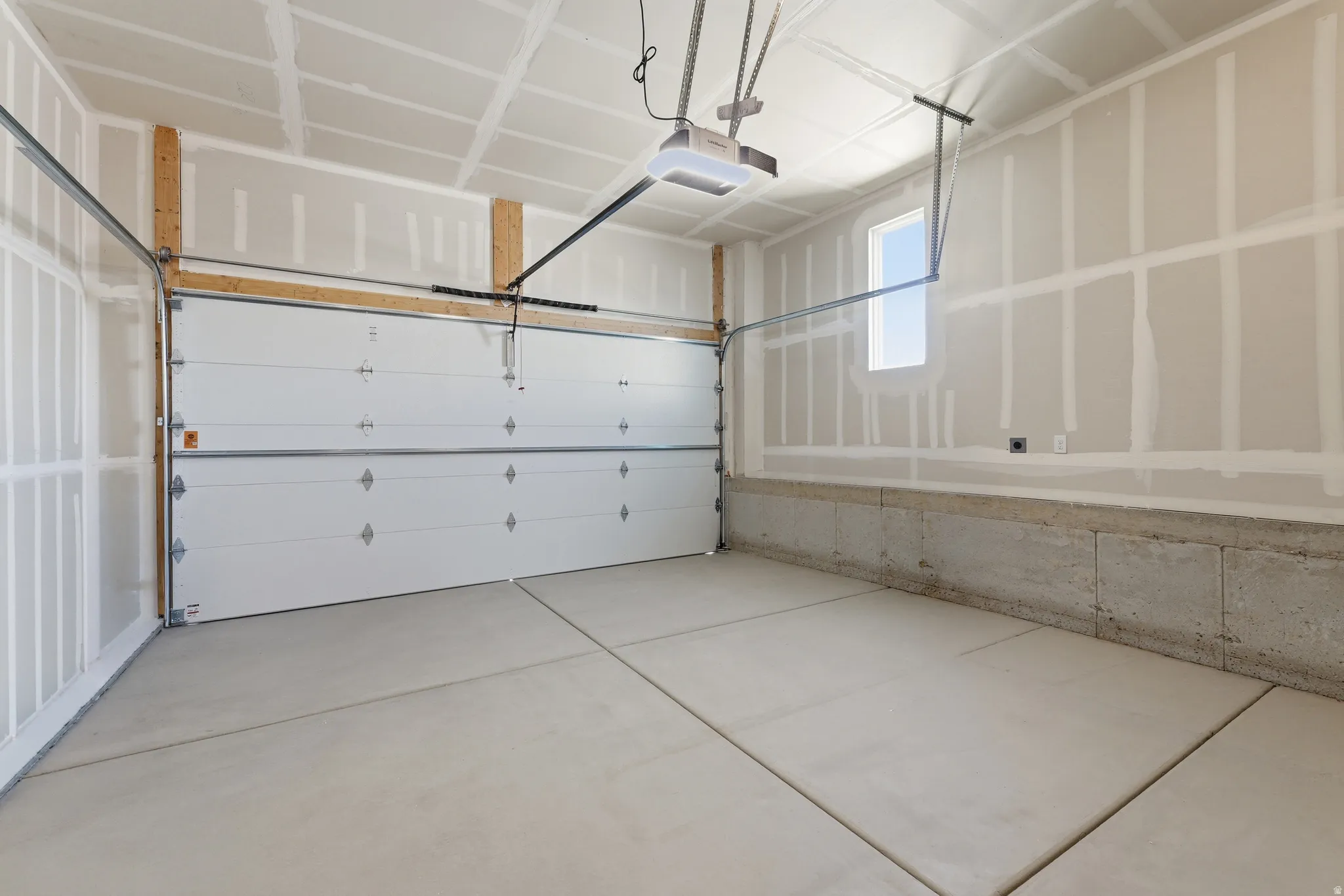 Spacious garage featuring a finished ceiling, drywall-ready walls, concrete flooring, a multi-panel overhead door, and an operable window
