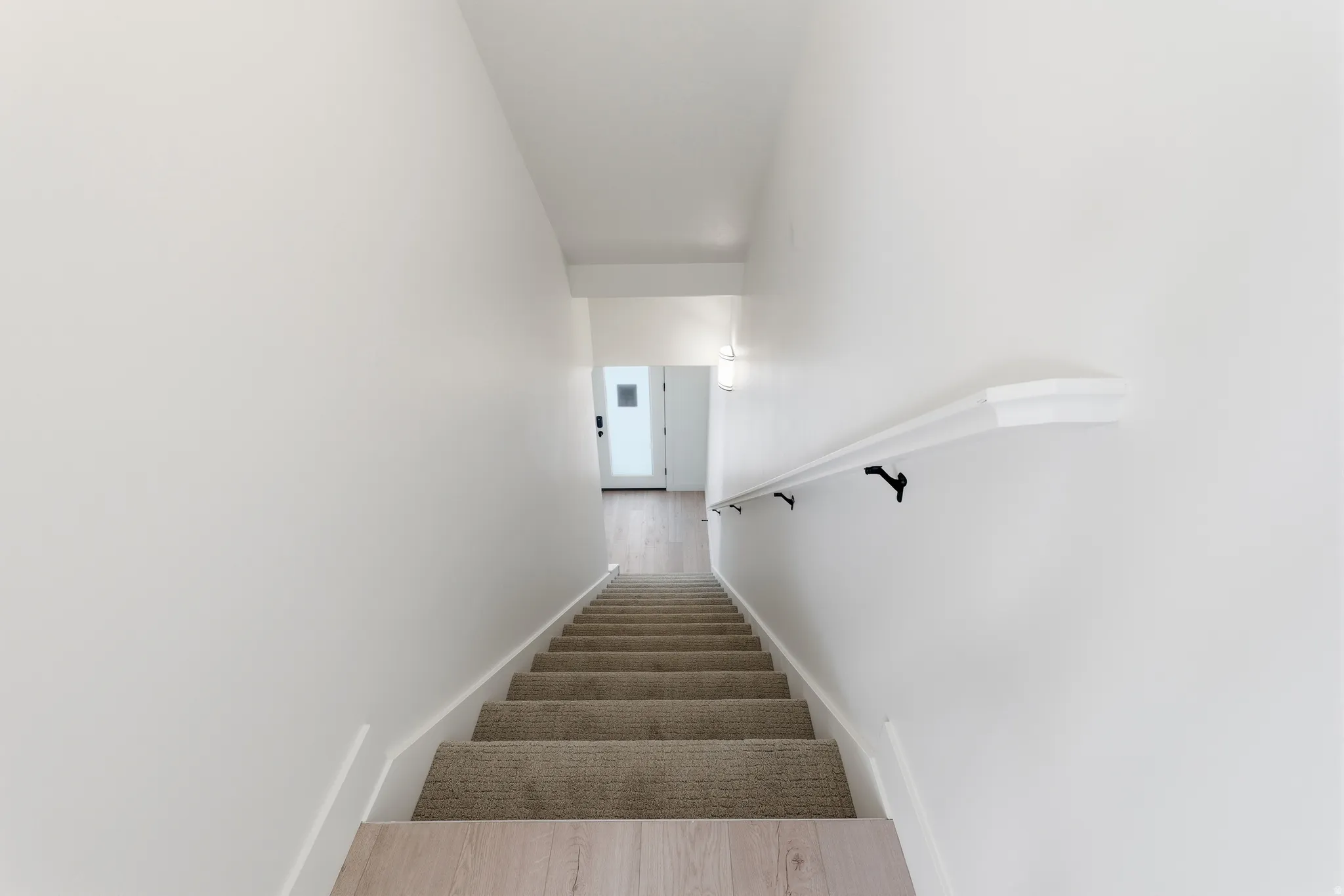 Carpeted staircase with white risers and light wood-finish treads, featuring a white handrail with black supports