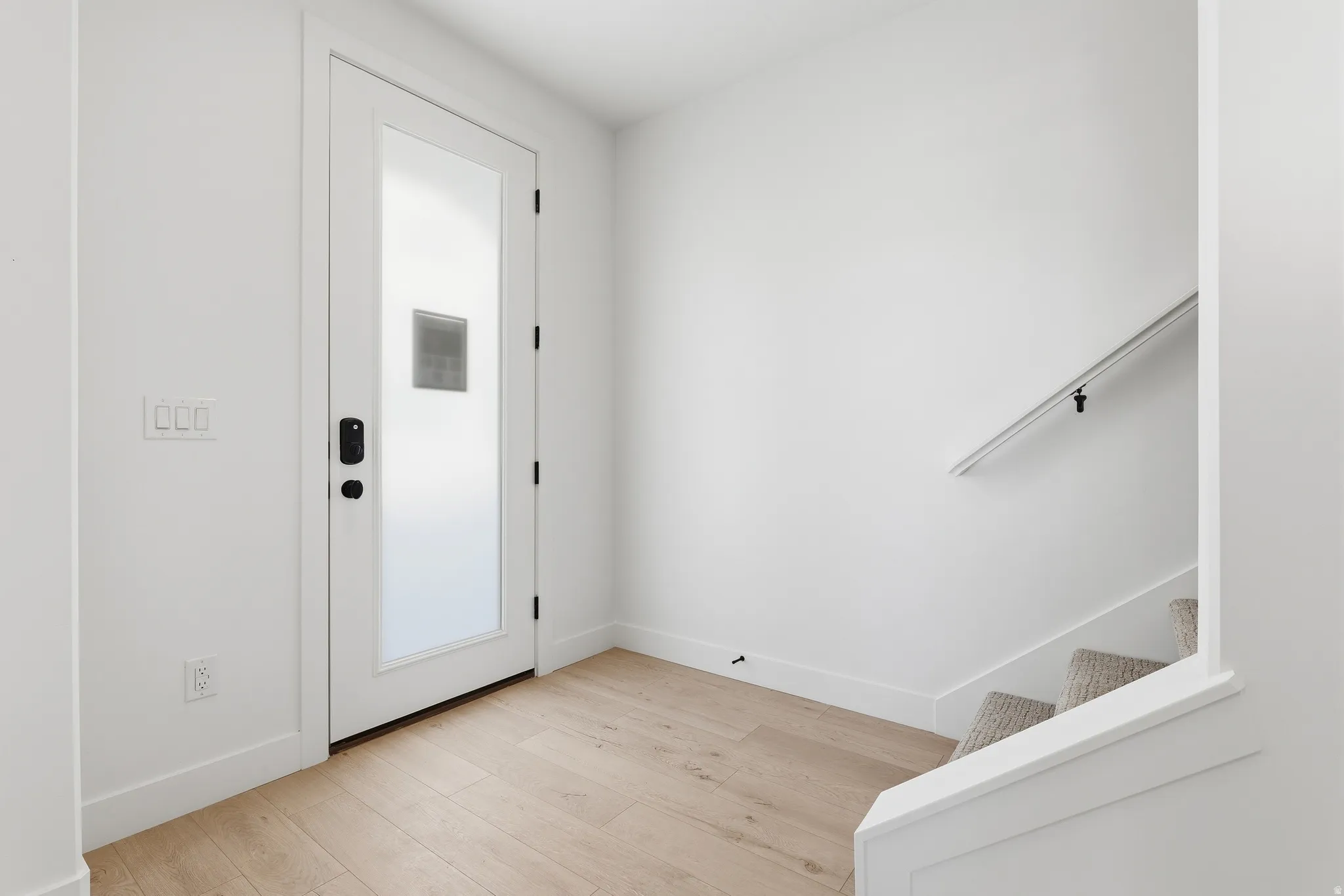 Entryway featuring a frosted glass door with smart lock, wood-finish flooring, a carpeted staircase with a white handrail, and crisp white walls