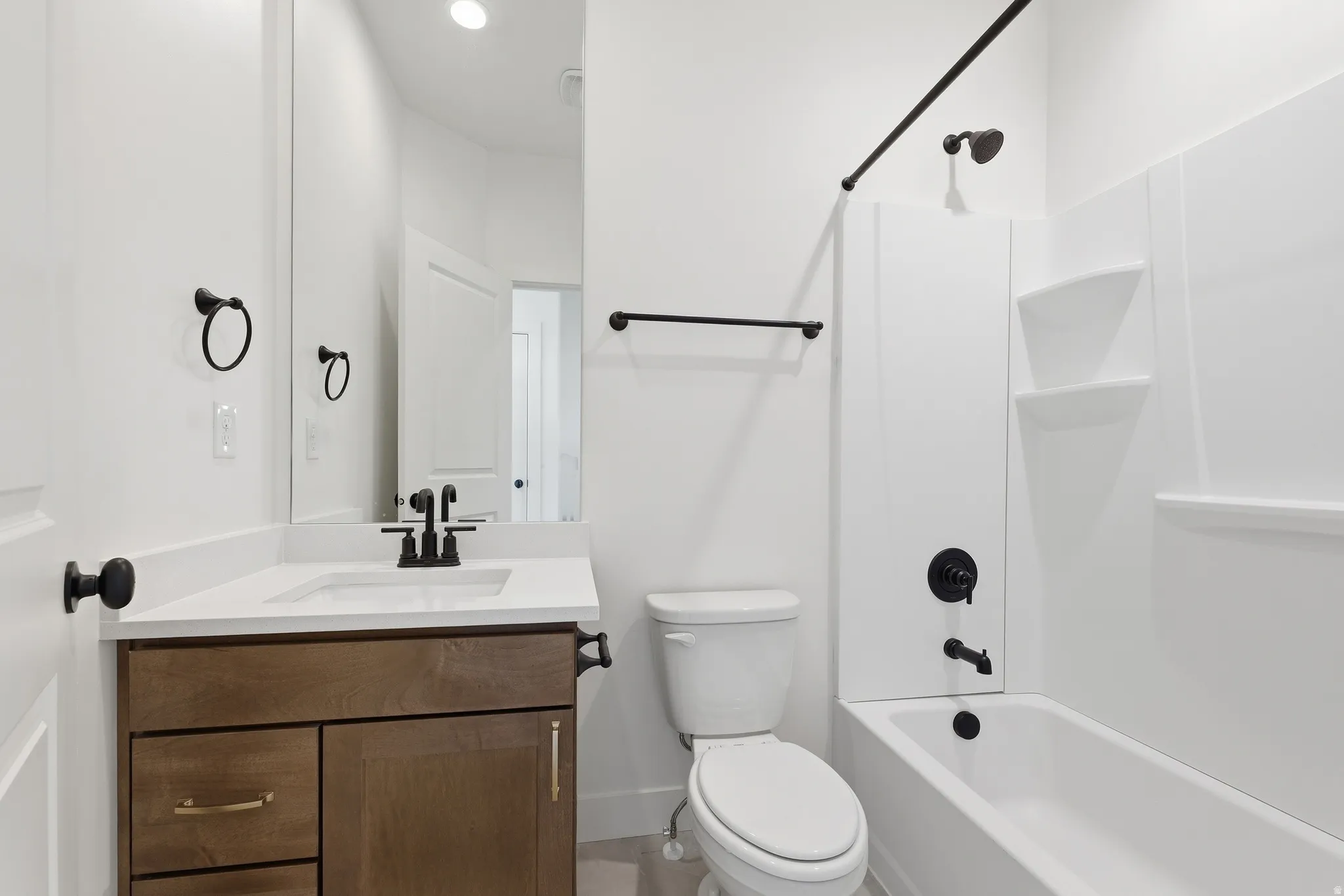 Bathroom featuring a wood-finish vanity with a light-toned countertop, a white toilet, and a white tub with integrated shelving