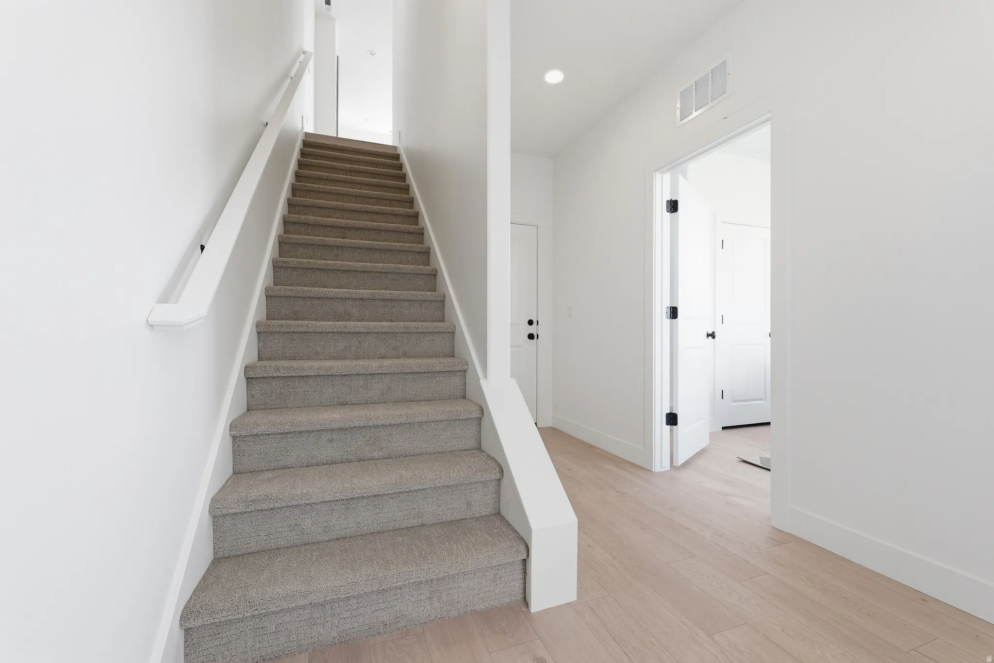 Carpeted staircase with white handrail and risers