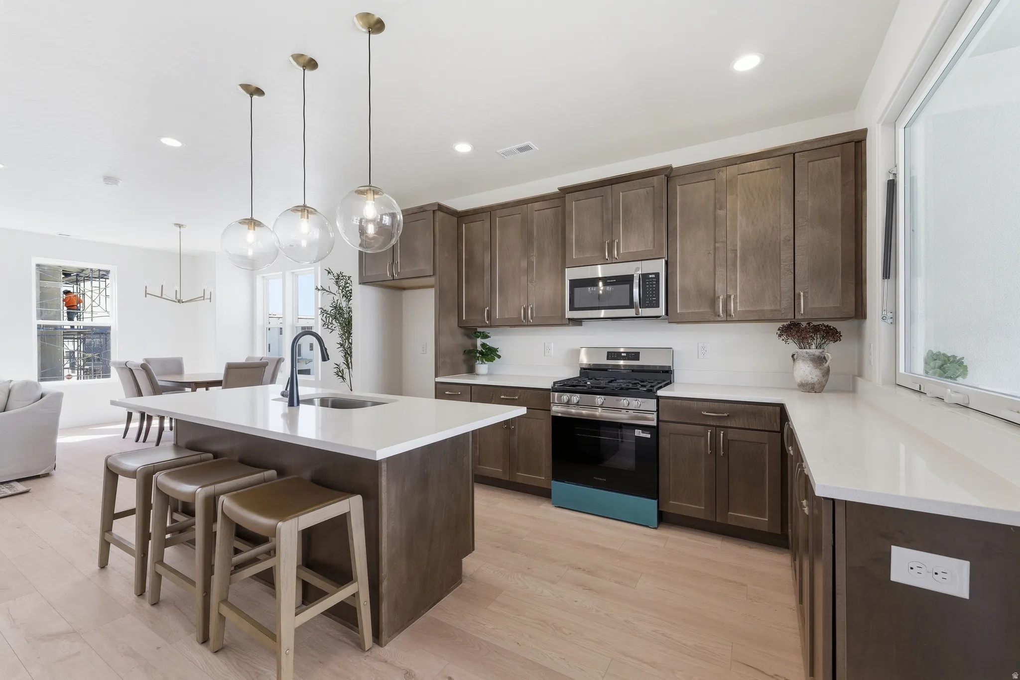 Open-concept kitchen featuring an island with seating, pendant lighting, stainless steel appliances, wood-finish flooring, and white countertops