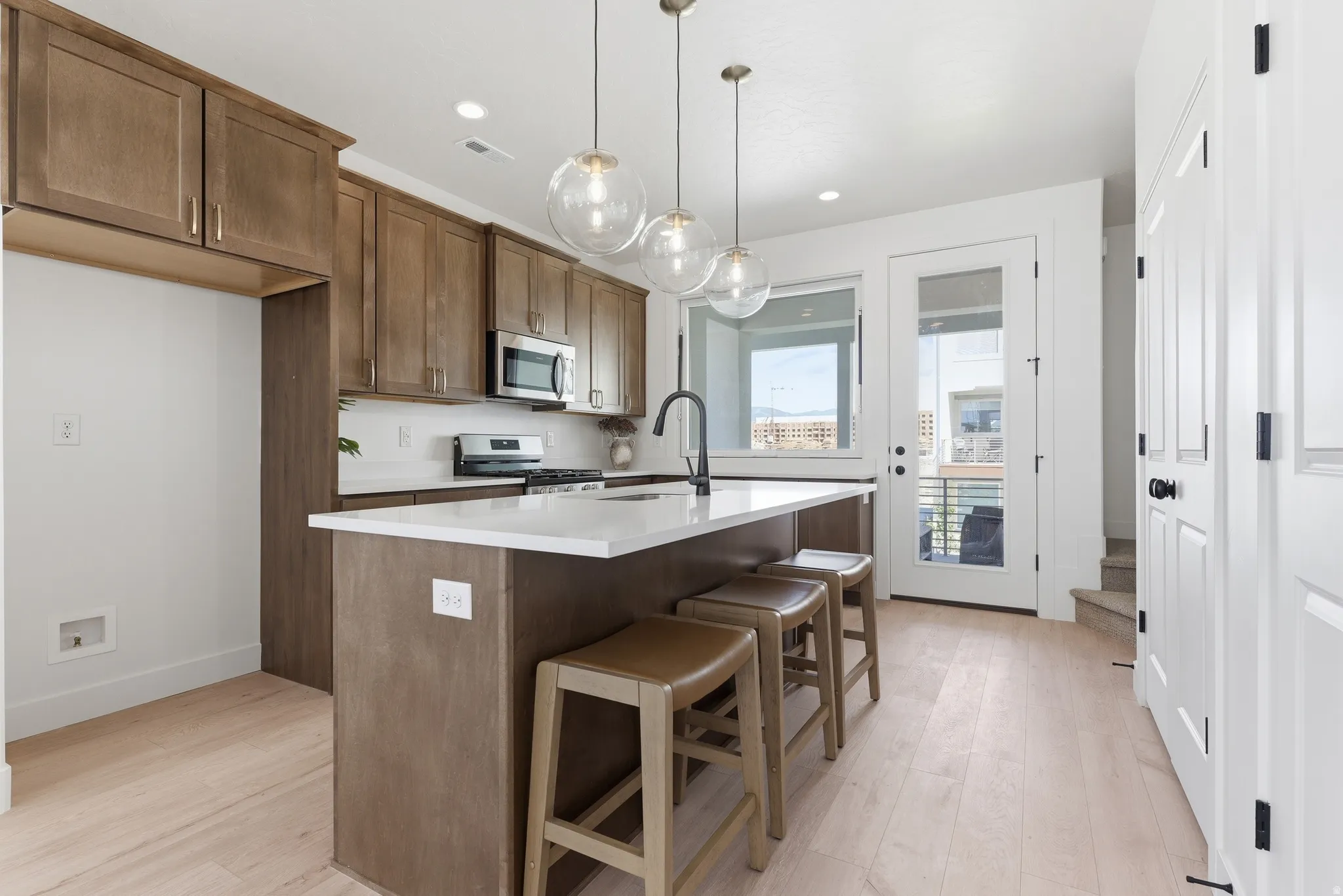 Modern kitchen featuring wood-finish flooring, a central island with a white countertop, a white subway tile backsplash, and light wood-tone cabinetry