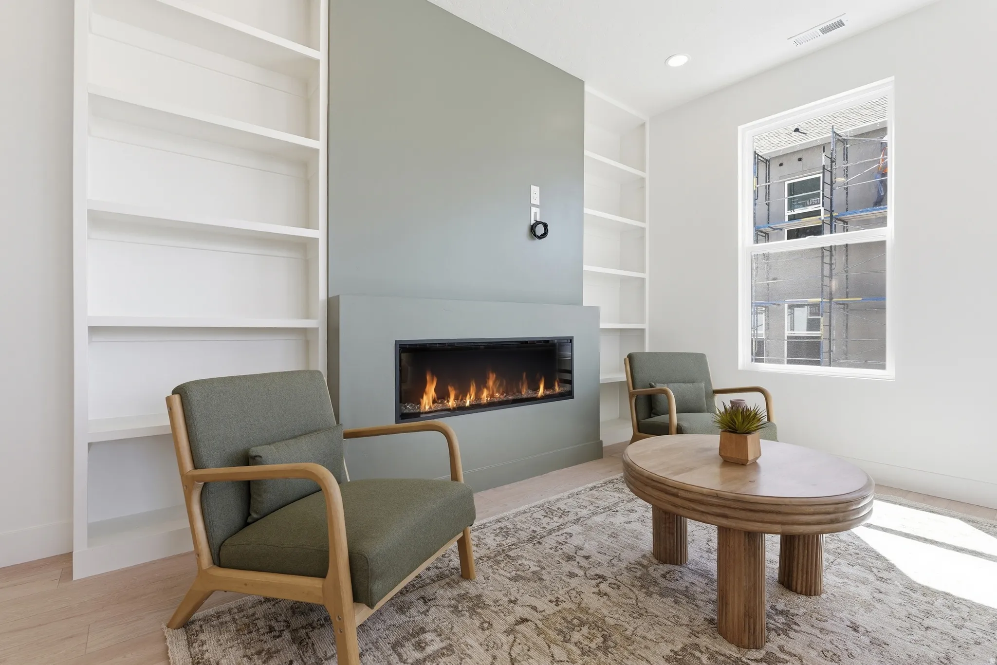Modern living area featuring a built-in electric fireplace, integrated shelving, bright white walls, and light wood-finish flooring