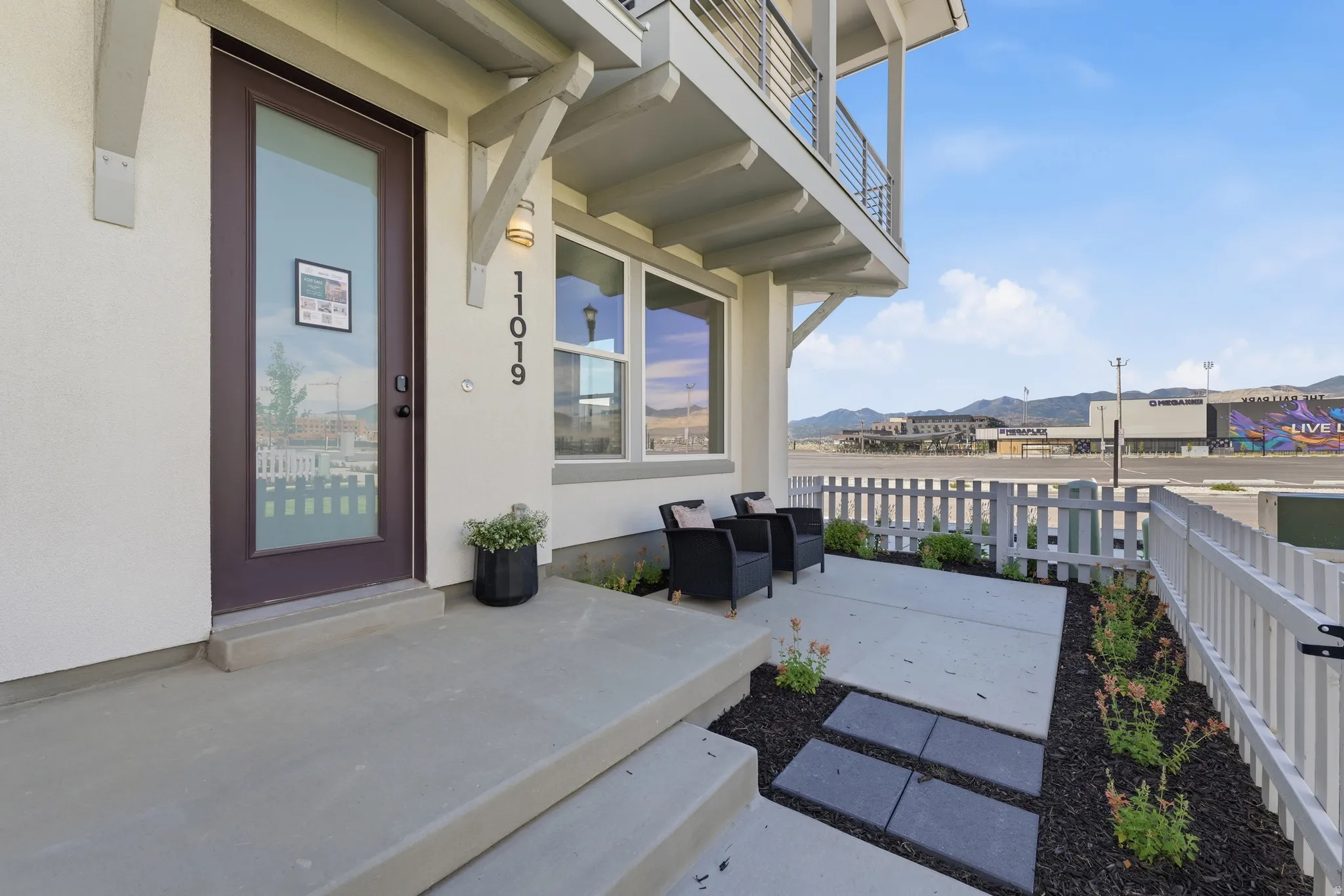 Contemporary exterior featuring a full-light entry door, a balcony with cable railings, a concrete patio, and a white picket fence