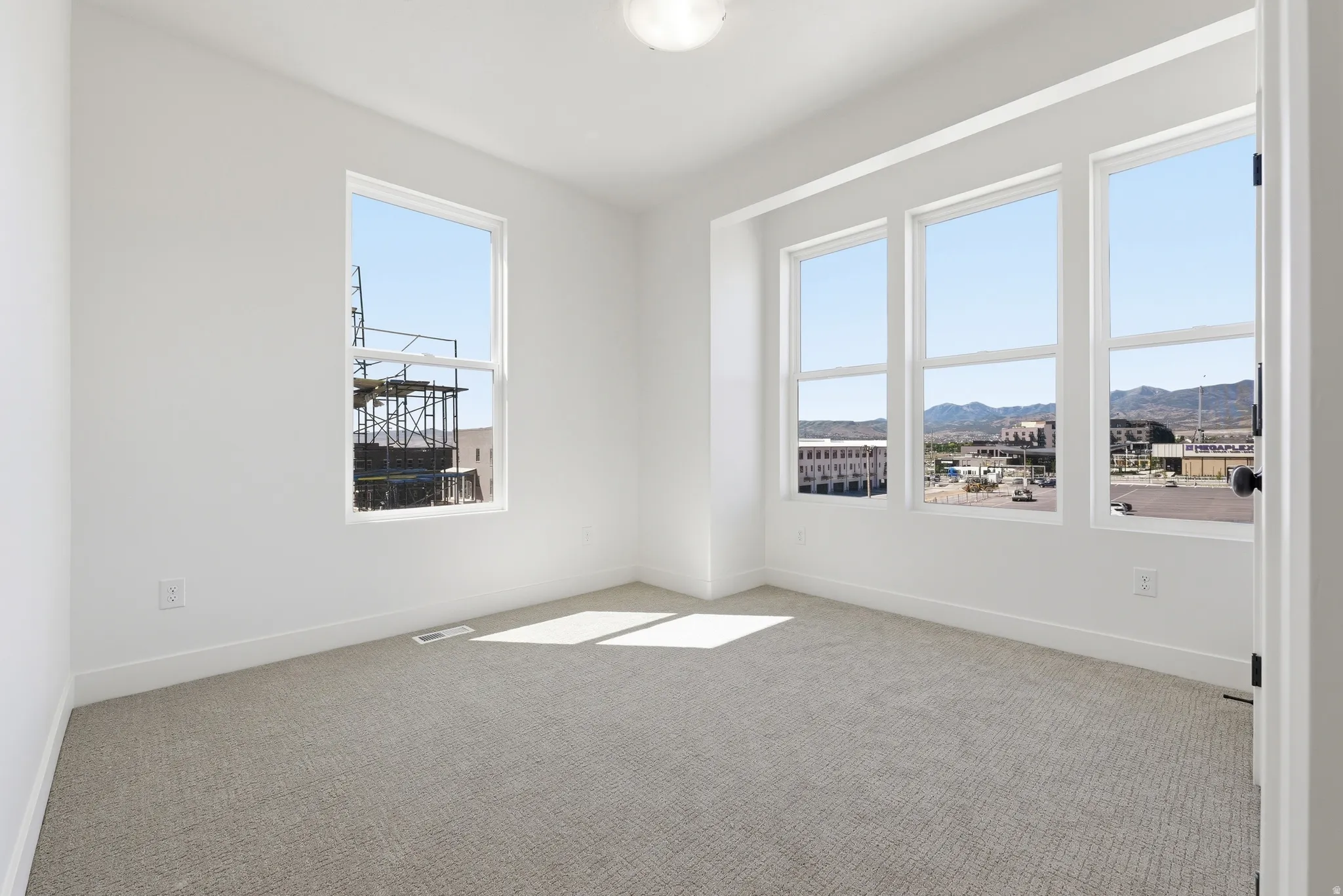 Bright interior room featuring neutral carpeting, white painted walls, and extensive window coverage