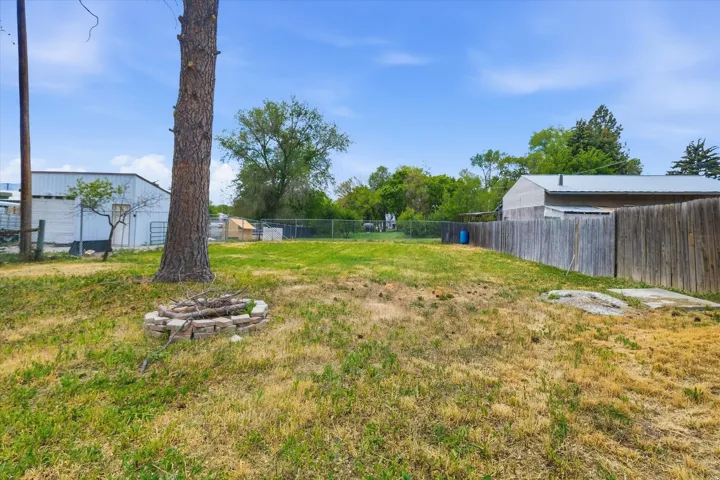 Expansive outdoor space featuring a stone-ringed fire pit, mature tree, and a wood privacy fence