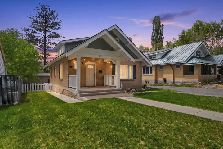 Brick facade home featuring a covered front porch with white railings, a front door with a window, and a neatly manicured lawn