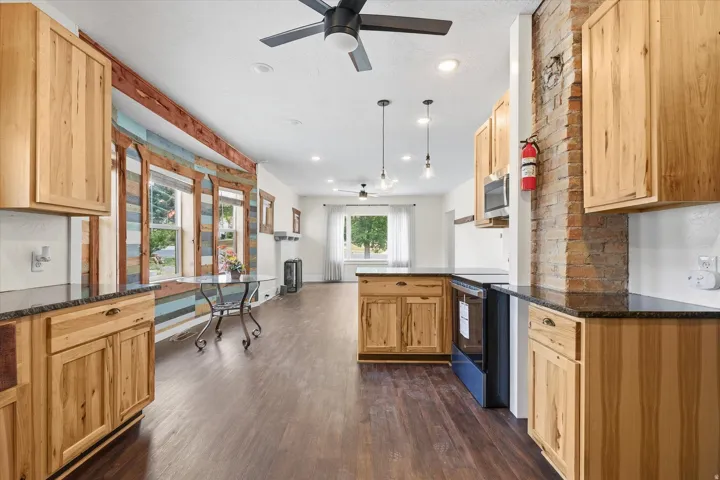 Modern kitchen featuring wood-finish cabinetry, dark countertops, built-in microwave, and electric range