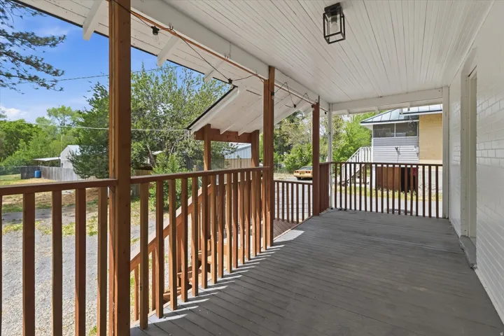 Covered back porch featuring a dark wood-finish deck, natural wood pillars, a coordinating wood railing, and a white beadboard ceiling with an attached lantern-style light fixture