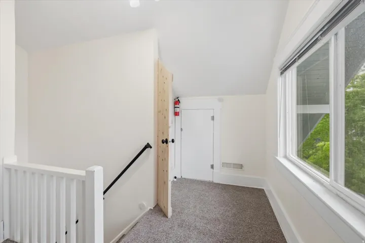 Upper-level landing featuring carpet flooring, crisp white walls, and a large multi-pane window