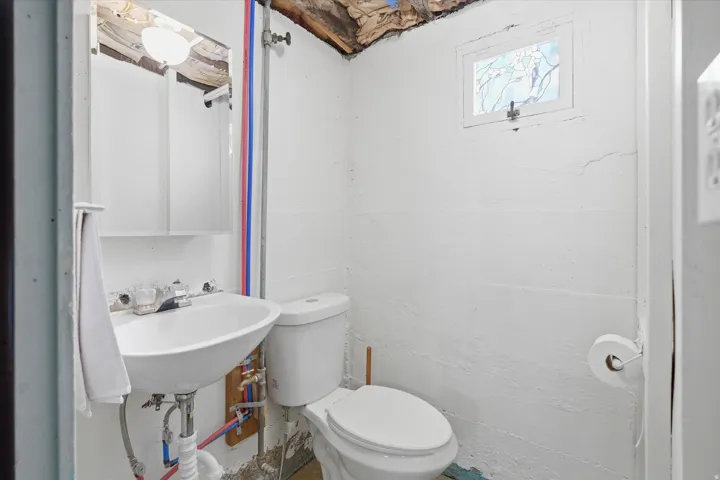 Compact bathroom featuring a pedestal sink, white toilet, and a small stained-glass window