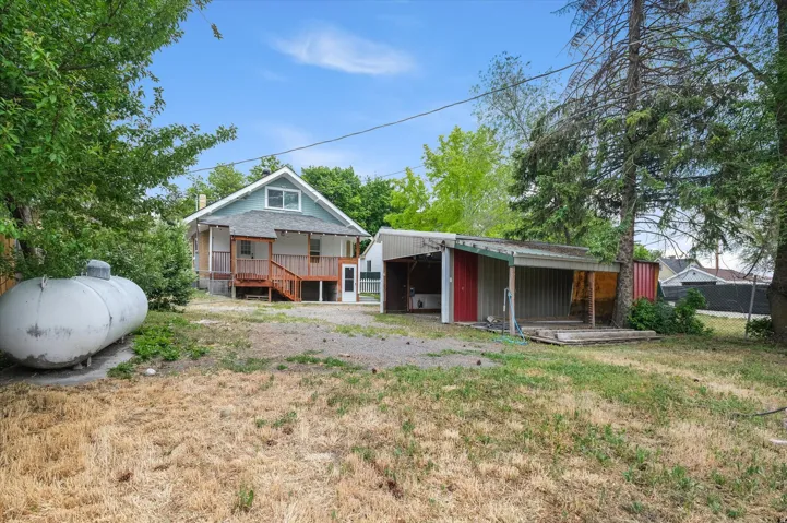 Rear exterior featuring a light blue siding, a deck with wood railings, and a gravel patio area