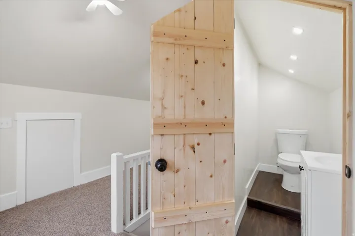 Sloped ceiling bathroom featuring recessed lighting, a white vanity with integrated sink, and wood-finish flooring