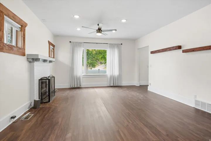 Spacious room featuring wood-finish flooring, a white brick fireplace with a mantle, and recessed ceiling lighting