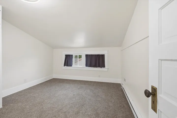 Carpeted room with a multi-pane window, white trim, and a sloped ceiling