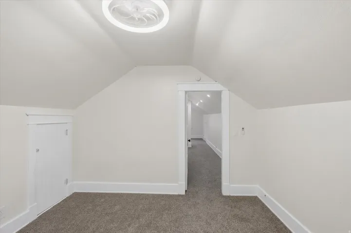 Carpeted room with sloped ceilings, white baseboards, and white wall paint