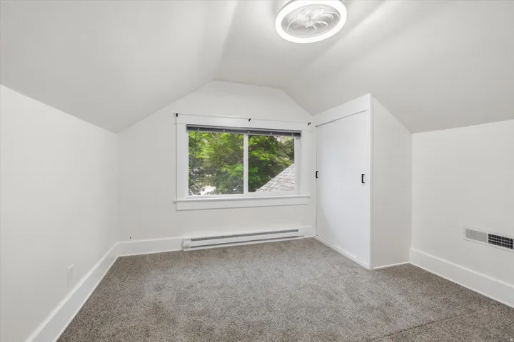 Attic space featuring sloped ceilings, a window with white trim, gray carpet flooring, and a built-in closet with sliding doors