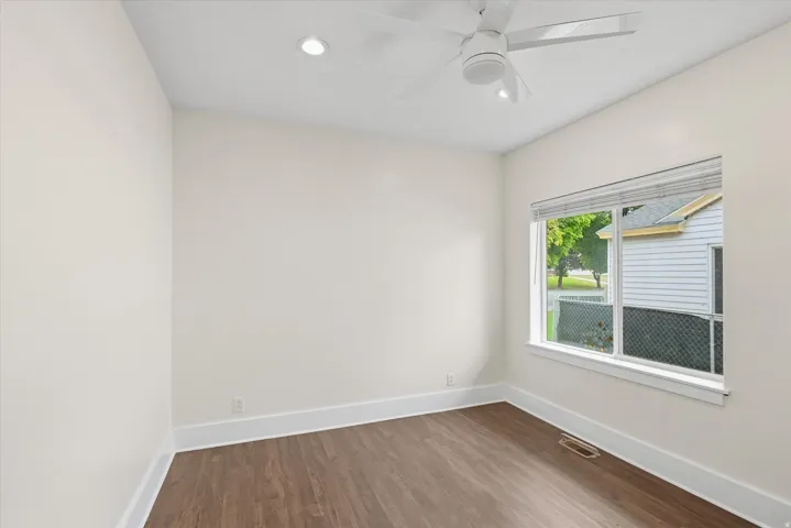 Spacious room featuring wood-finish flooring, white baseboards, a large window with blinds, recessed lighting, and a ceiling fan